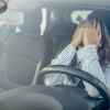 A woman sitting in the driver's seat of a car covering her face with her hands