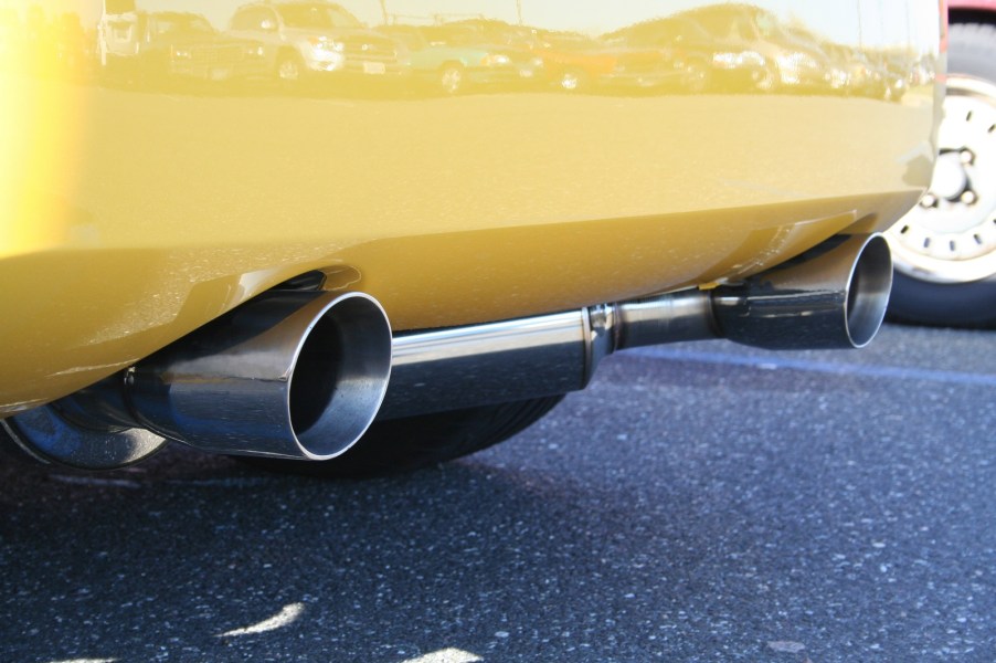 A yellow car's rear bumper shows dual exhaust tips close to the road