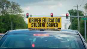 A car with a sign on the roof that says "driver education student driver" in bold lettering