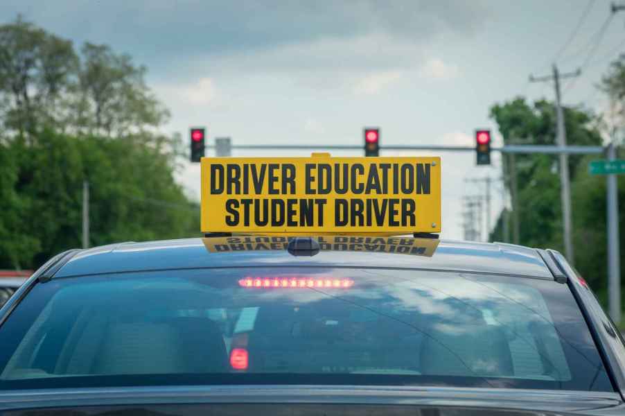 A car with a sign on the roof that says "driver education student driver" in bold lettering