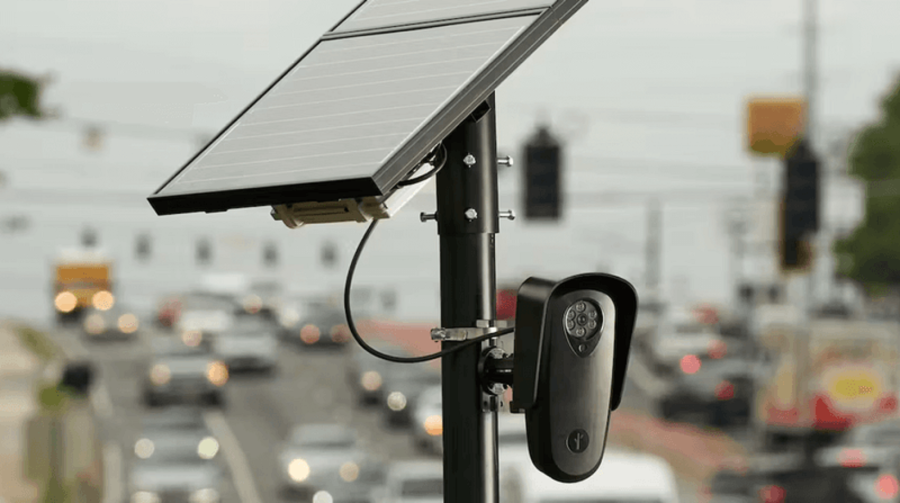 A Flock Safety automatic license plate recorder (ALPR) is shown installed on a roadway with blurred traffic in the background