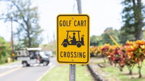 Bright yellow "Golf Cart Crossing" sign with a golf cart visible in the background.