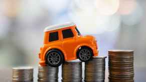 Representation of car loan interest rates by a toy car positioned on stacks of silver coins on tabletop