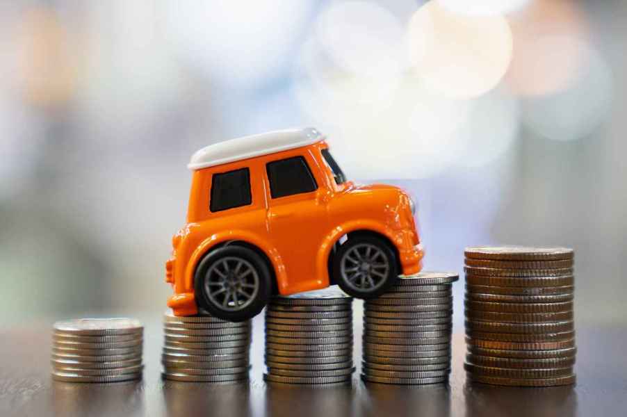 Representation of car loan interest rates by a toy car positioned on stacks of silver coins on tabletop