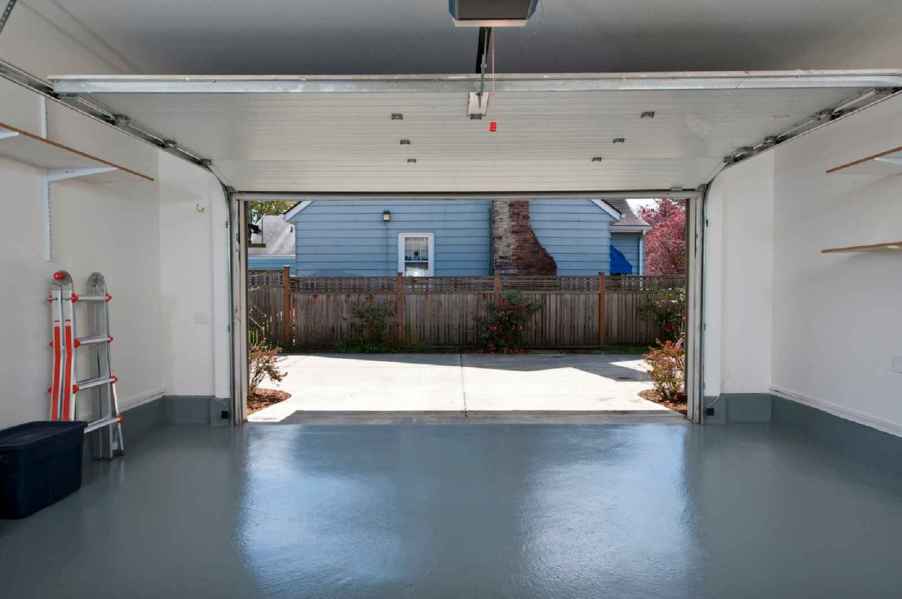 The view from inside a cleaned out garage with the door open gray painted floor folded up ladder on left side