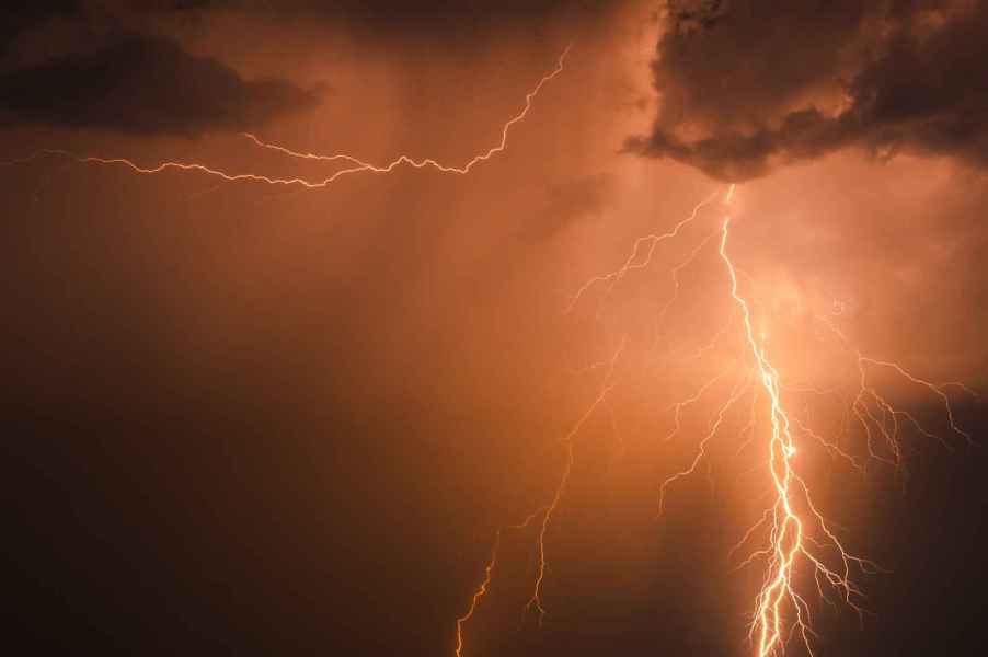 Orange lightning bolts striking a black-colored sky and clouds