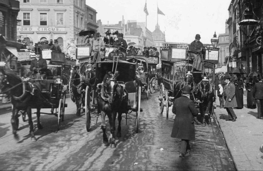 A black and white image of London traffic circa 1870 featuring horse drawn carriages and pedestrians