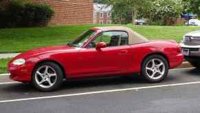 A red Mazda Miata roadster with brown canvas convertible top parallel parked on a street