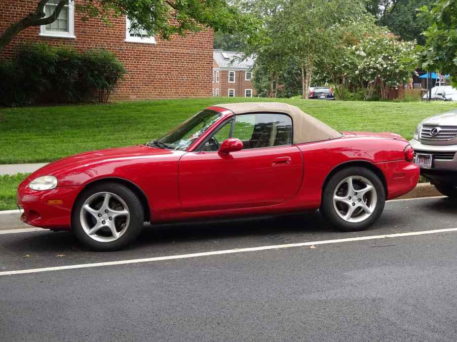 A red Mazda Miata roadster with brown canvas convertible top parallel parked on a street