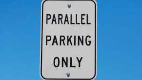 A white "parallel parking only" sign with blue sky background