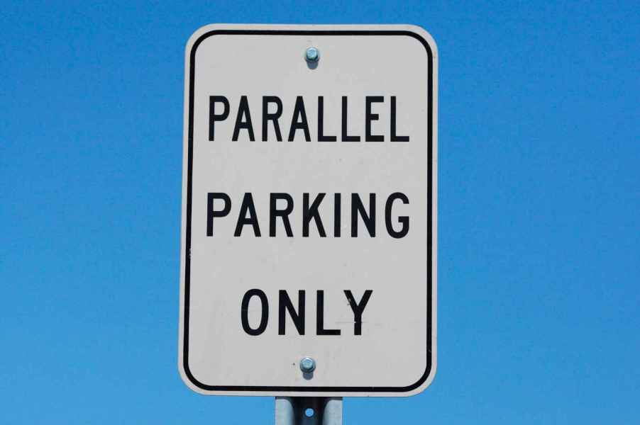 A white "parallel parking only" sign with blue sky background