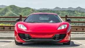 A red 2012 McLaren 12C coupe sits in direct front view green mountains in the background