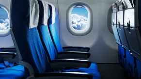 Airplane passenger seats facing right profile with round airplane window showing blue cloudy sky