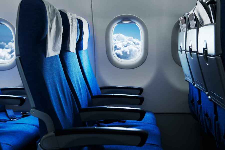 Airplane passenger seats facing right profile with round airplane window showing blue cloudy sky