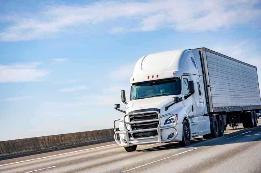 A white semi-truck driving down a highway with blue cloudy sky above