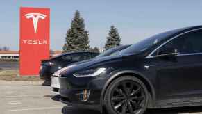 A red Tesla sign with a row of Tesla cars parked in a lot