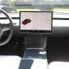 The steering wheel and info screen of a Tesla EV view from rear passenger area