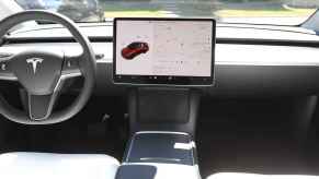 The steering wheel and info screen of a Tesla EV view from rear passenger area