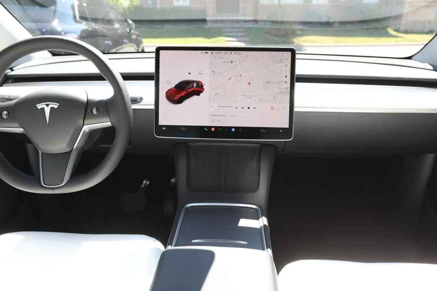 The steering wheel and info screen of a Tesla EV view from rear passenger area