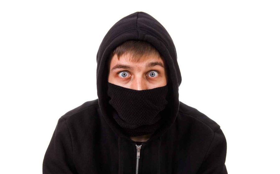 A depiction of a wide-eyed thief wearing black mask covering nose and mouth and black hoodie sweatshirt blue wide eyes looking straight at viewer