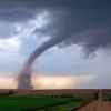 A full tornado shown touching down in a rural scene with a dirt road to the right frame