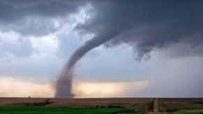 A full tornado shown touching down in a rural scene with a dirt road to the right frame