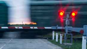 A train passing a crossing with red traffic signal and arm down at dusk