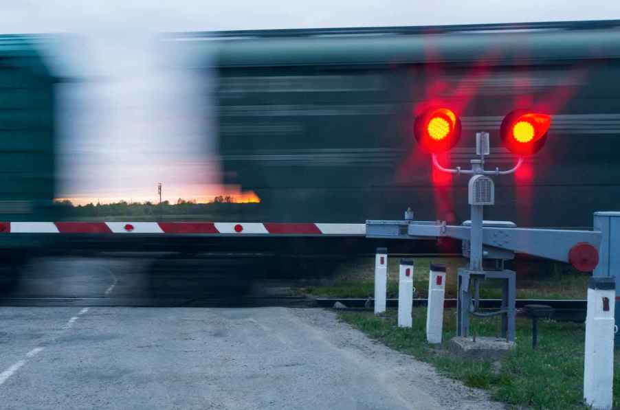 A train passing a crossing with red traffic signal and arm down at dusk