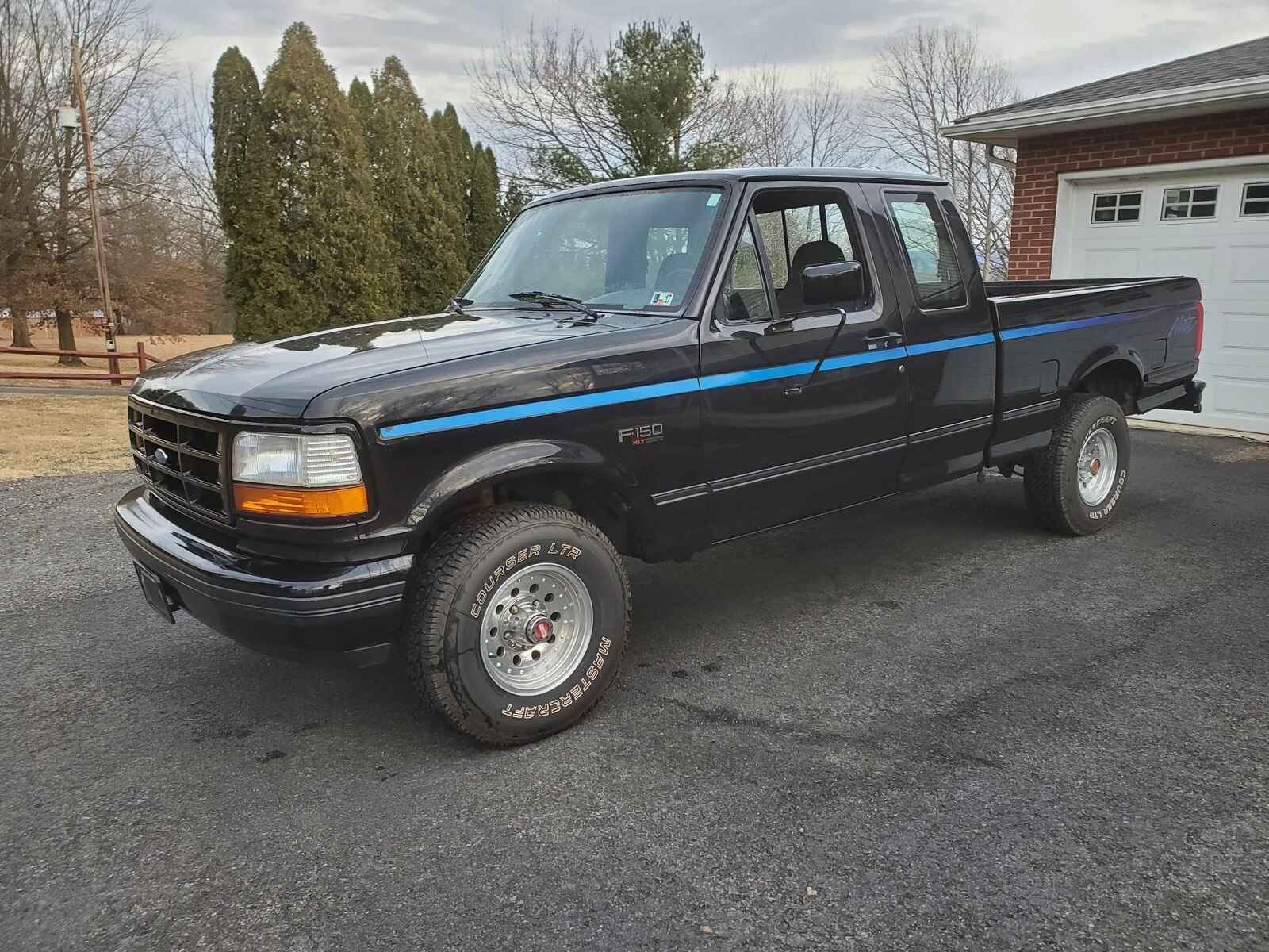 A black 1992 Ford F-150 Nite Edition with signature blue pinstripe down the side parked in left front angle view