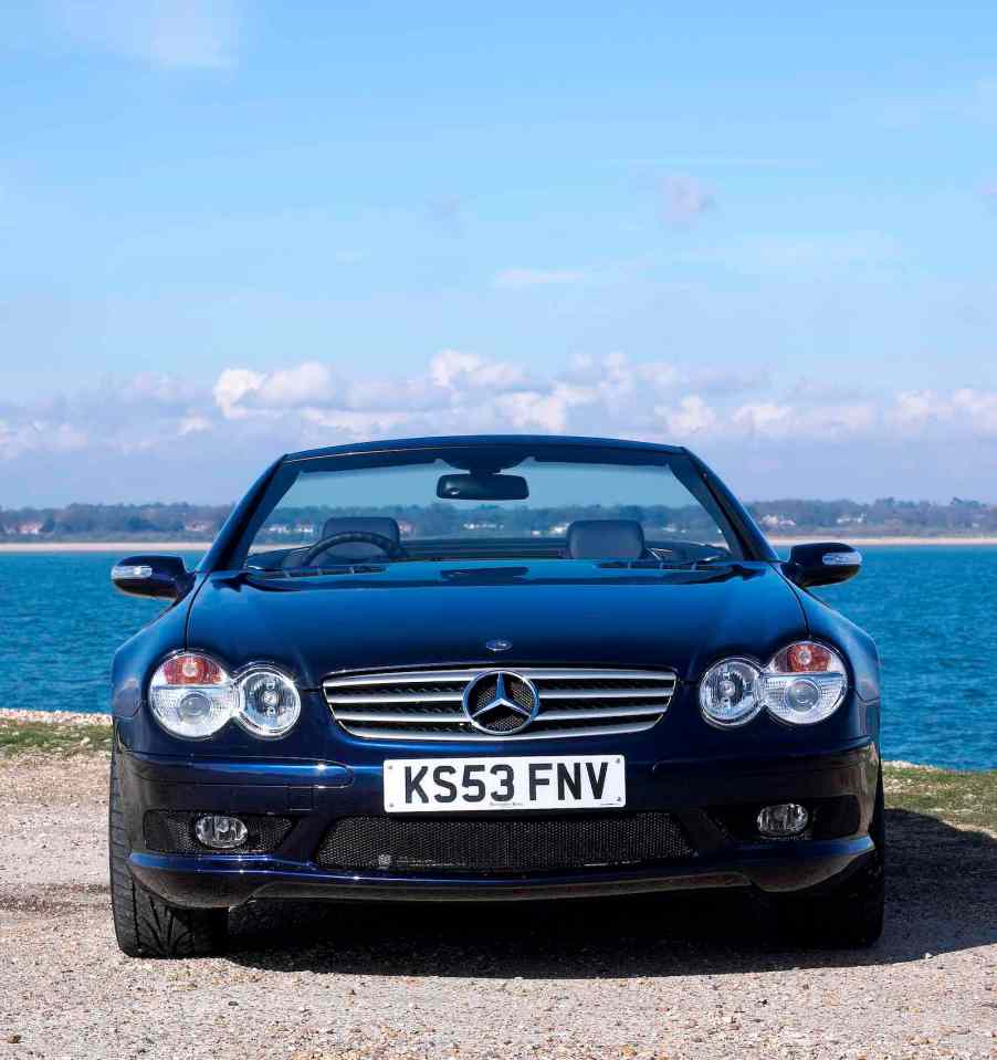 Mercedes-Benz supercar convertible parked in front of a blue ocean with its top down.