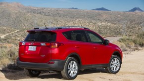 A red example of a 2013-2015 Toyota RAV4 SUV parked in a dry desert environment away from the road in right rear angle