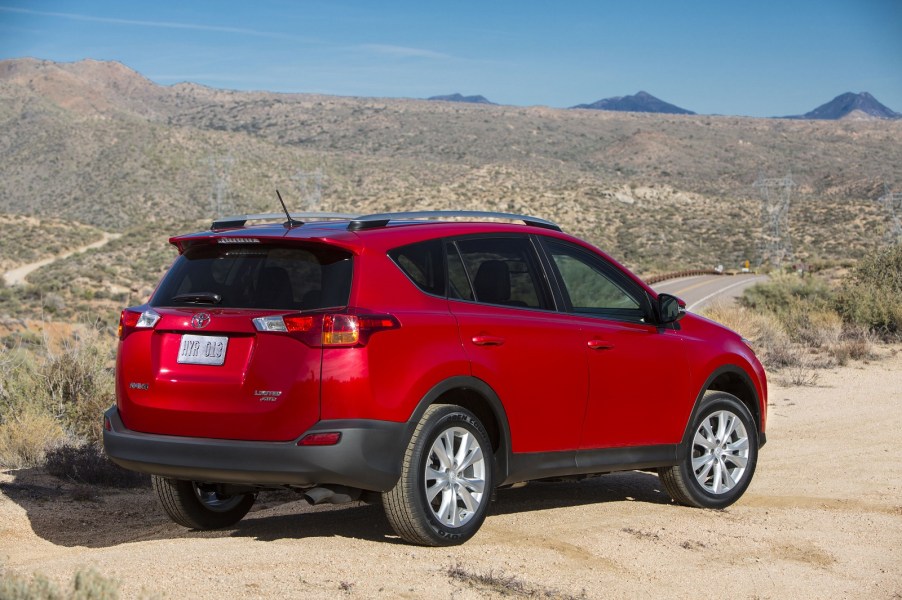 A red example of a 2013-2015 Toyota RAV4 SUV parked in a dry desert environment away from the road in right rear angle