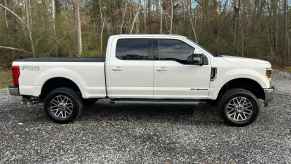 A white Ford F-250 parked on gravel in right profile view