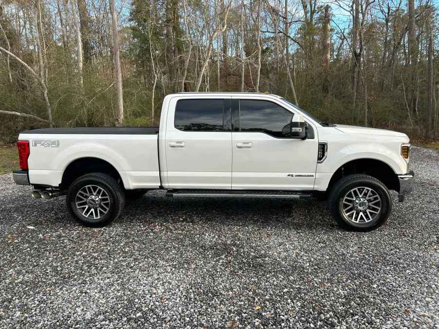 A white Ford F-250 parked on gravel in right profile view