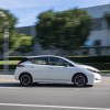 A white Nissan LEAF drives down an empty street.