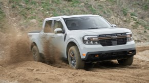 A light grey 2023 Ford Maverick in right front angle view off-roading with dry dirt spraying from right side wheels