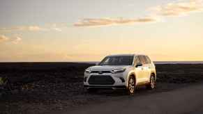 A white 2024 Toyota Grand Highlander SUV parked outside in semi-distant midground in left frotn angle view at sunset