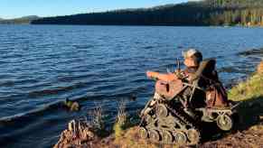 Man fishes from a lakeshore while sitting in an all-terrain trackchair.