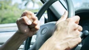 A driver with road rage clenches their fist behind the wheel of a car.