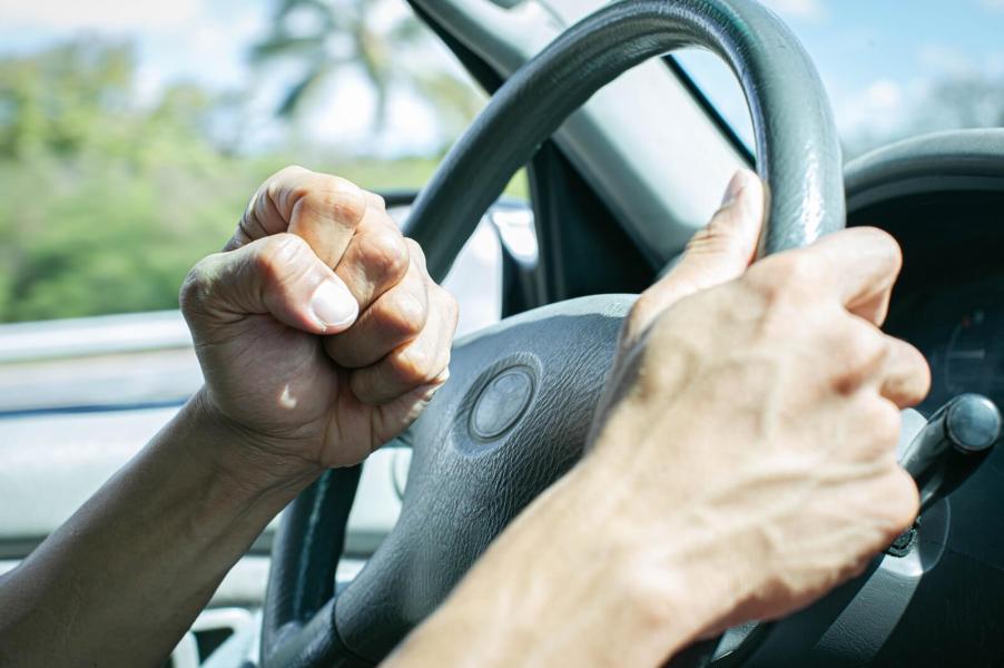 A driver with road rage clenches their fist behind the wheel of a car.