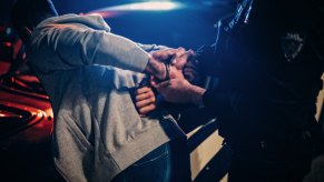 A police officer arrests a driver by their vehicle.