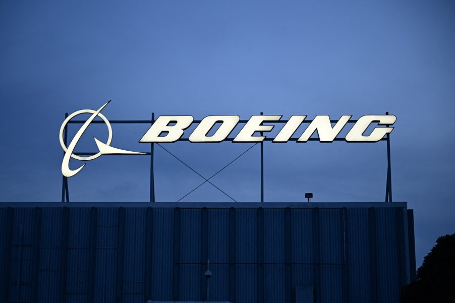 The illuminated Boeing logo on the roof of a dark building at sunset.