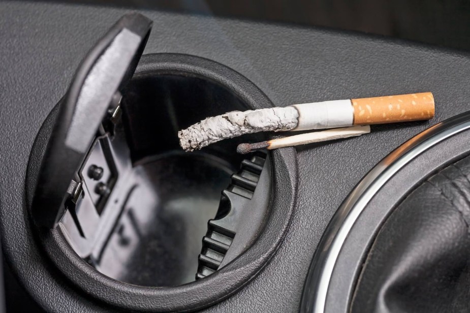 Cigarette balancing on the ashtray of a car's center console.