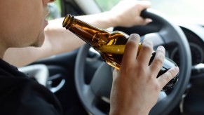 A man drinks from a glass bottle of beer while driving a car.