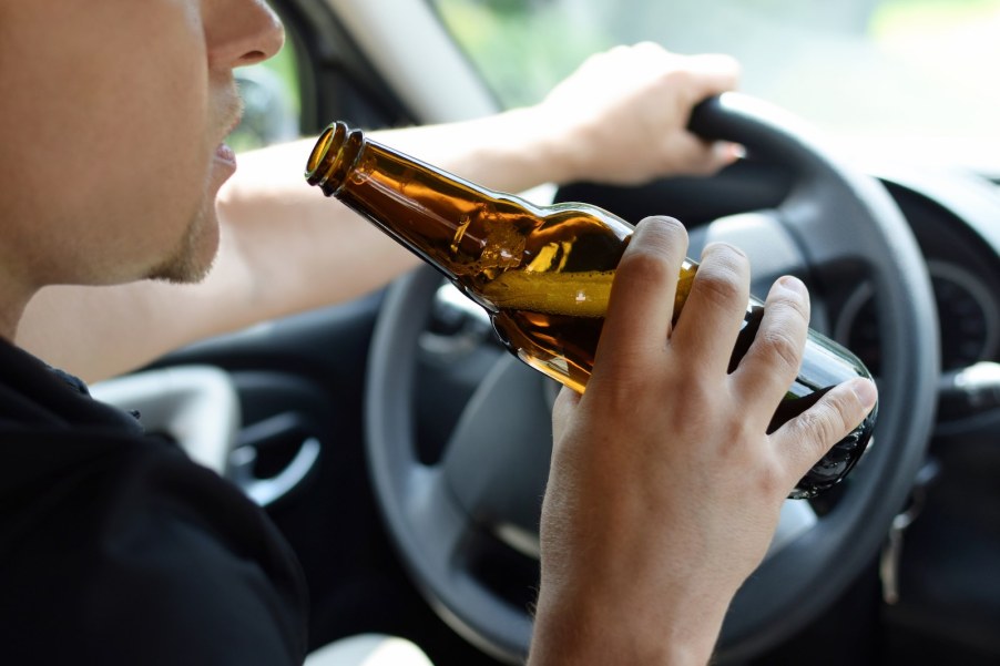 A man drinks from a glass bottle of beer while driving a car.