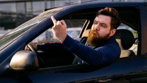 Bearded man giving the middle finger out an open car window.