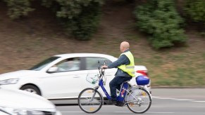 Man rides an e-bike through traffic, a white car visible in the background.