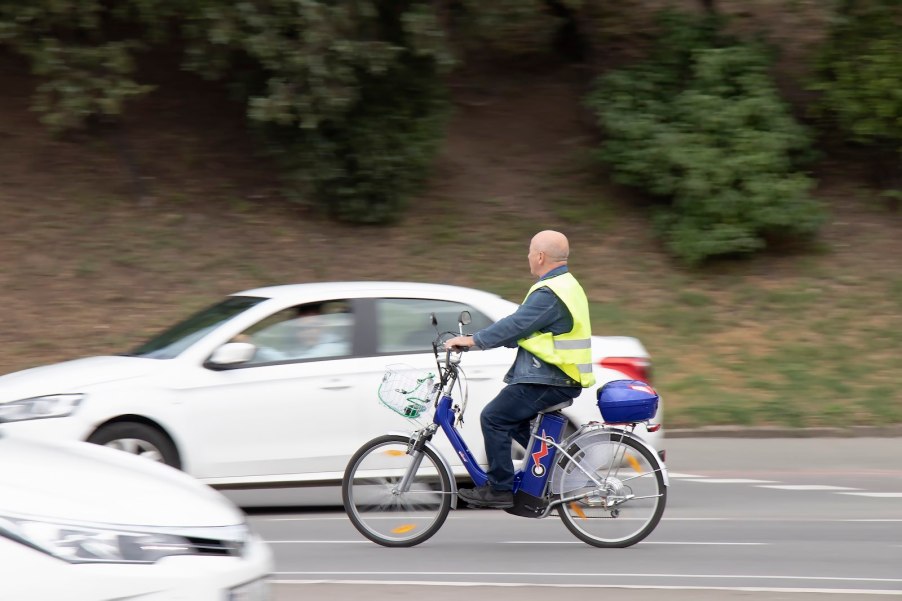 Man rides an e-bike through traffic, a white car visible in the background.