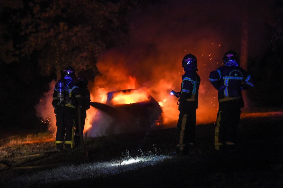 Three firefighters use a hose to extinguish a burning car