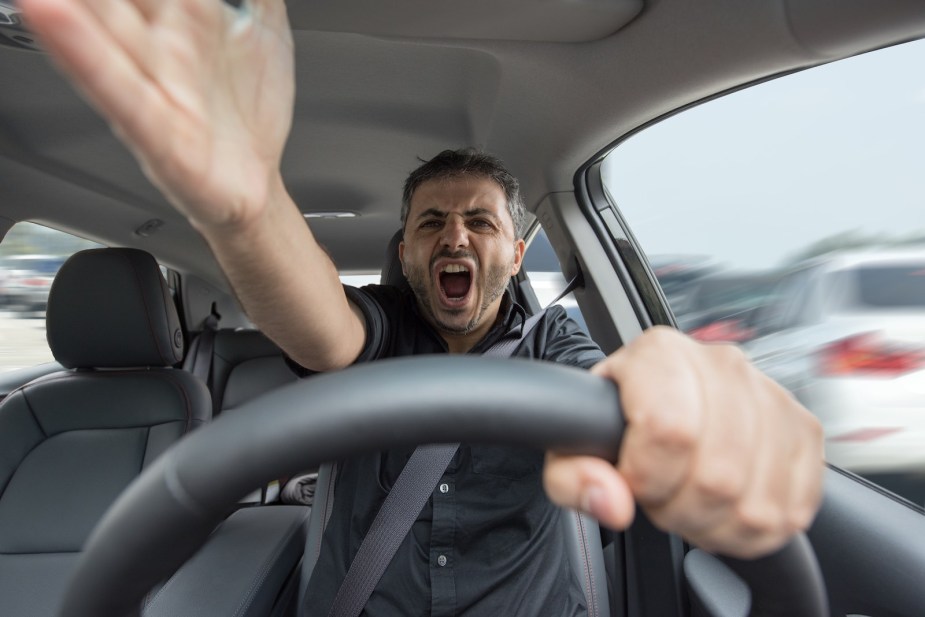 Road rage driver points and yells behind the wheel.